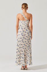 A woman is wearing a long, flowing dress with a beige base color and a blue floral print. The dress features a one-shoulder strap design. The fabric appears lightweight and comfortable, suitable for warm weather. She is also wearing neutral-colored high heels.